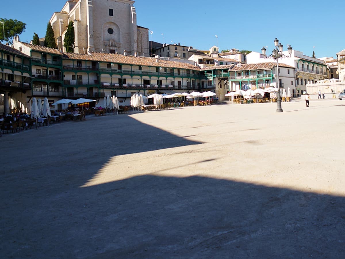 The arcaded main square of Chinchón, Spain, with balconies above and café terraces under parasols along one side.