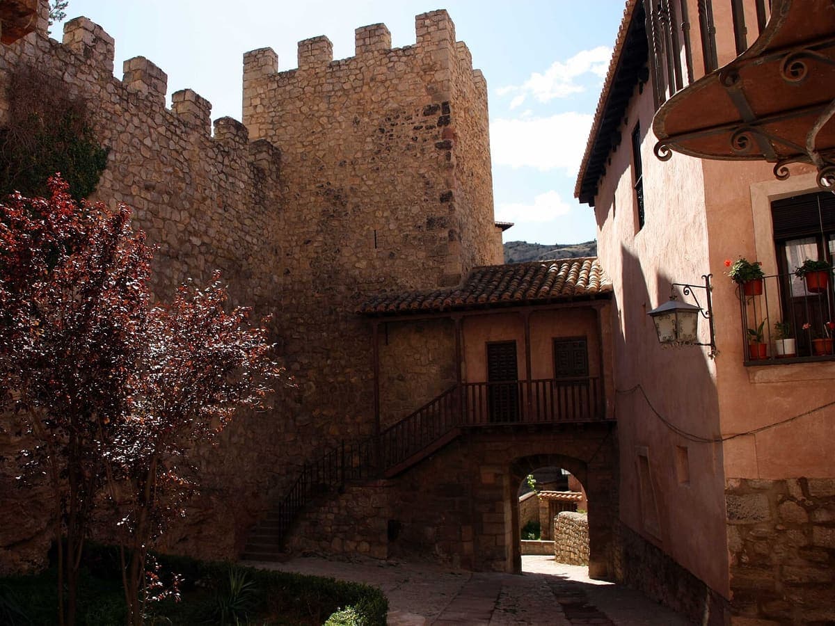 A corner of Albarracín, Teruel: a wooden gallery under a tiled roof beside the town wall, geraniums in pots on a balcony.