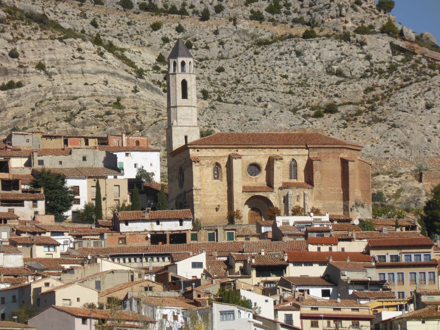 Castellote, in the province of Teruel, Spain: terracotta rooftops packed tightly below the parish church and a limestone cliff.