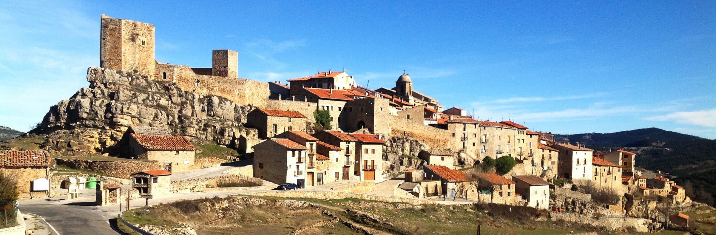 Puertomingalvo, in the province of Teruel, Spain: stone houses and terracotta roofs strung along a ridge beneath a castle tower.